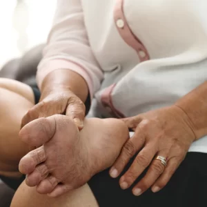 Mulher idosa examinando os próprios pés ressecados, destacando a importância do cuidado diário para prevenir feridas em pés diabéticos.