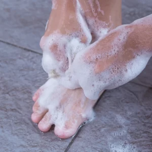 Pessoa lavando cuidadosamente os pés com sabão, ressaltando a importância da higiene para prevenir micose.