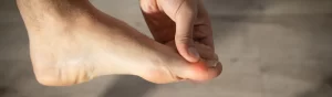 Pessoa segurando o dedão do pé com vermelhidão na lateral da unha, indicando um possível caso de unha encravada.